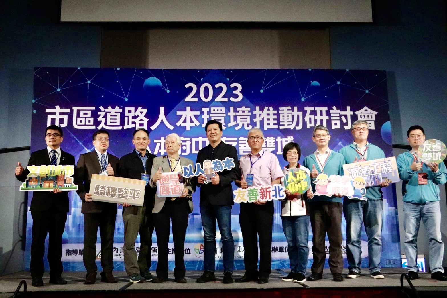 新北市副市長朱惕（中）、工務局長祝惠美（右4）、養工處長簡必琦（右3）與產官學界學者拿著以友善通行環境為主的舉手牌們，一同合影留念。